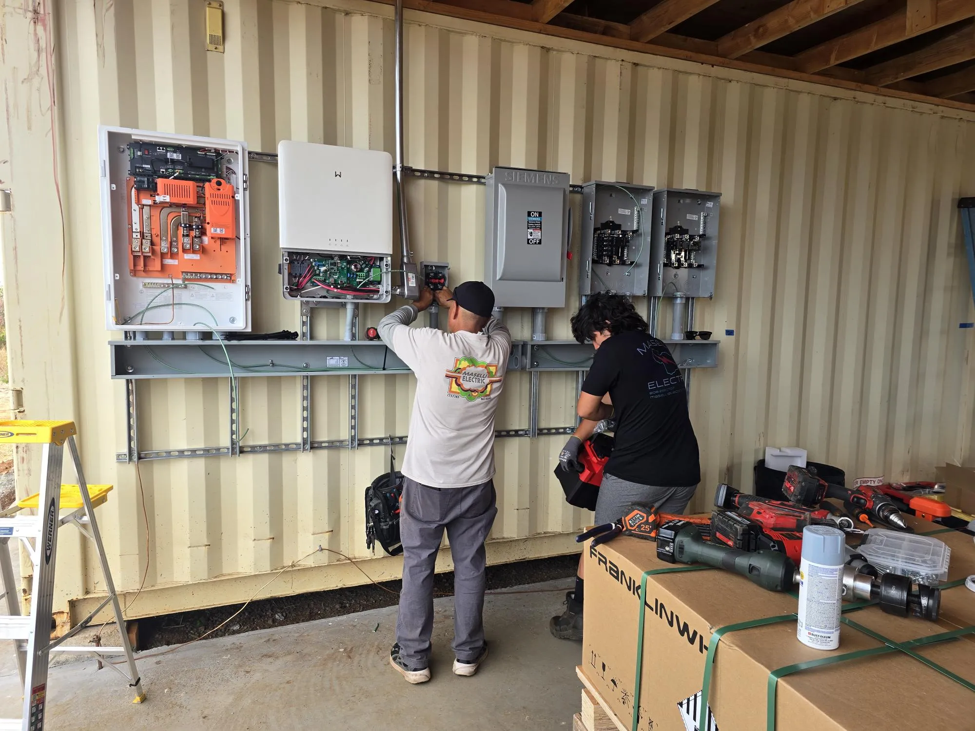 Two Maselli electricians in company shirts wiring an equipment wall
